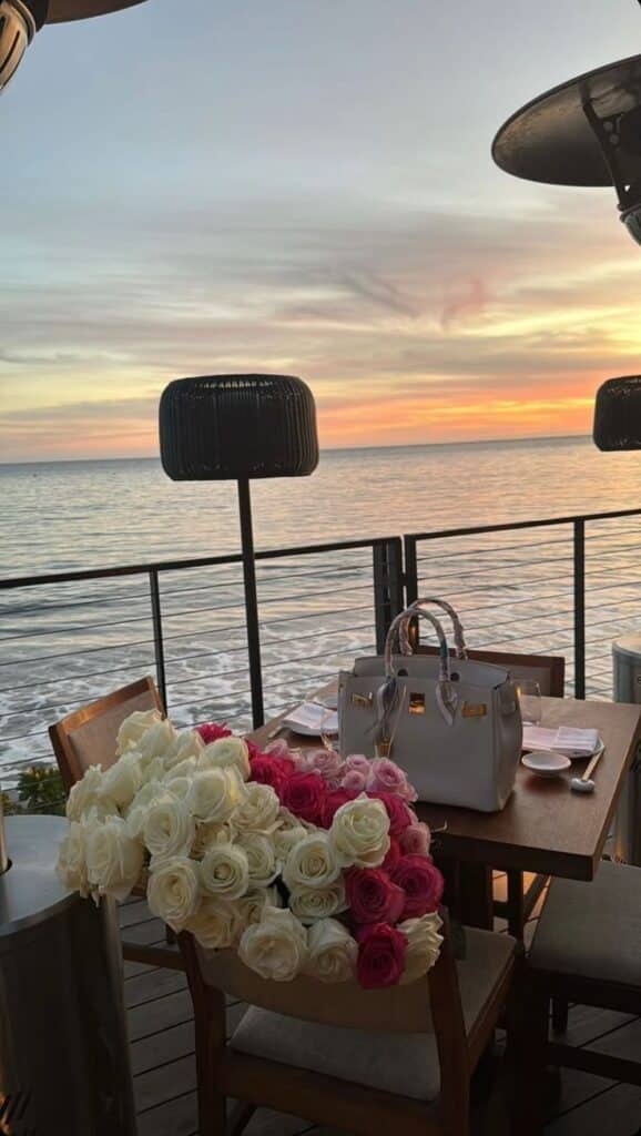 Roses and handbag on a table by the sea at sunset, creating a romantic dining ambiance.