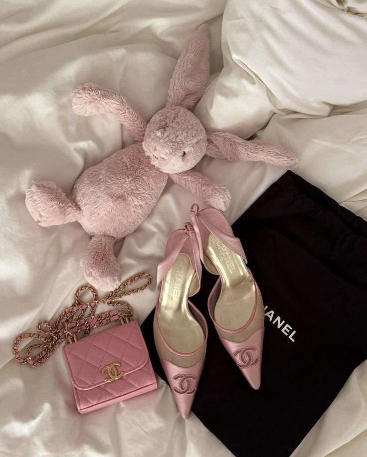 Pink Chanel shoes and purse with a plush bunny on a bed.