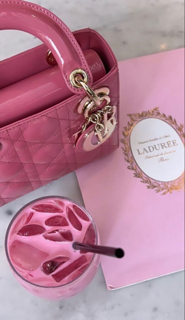 Pink designer handbag with Ladurée gift bag and iced pink drink on marble table.