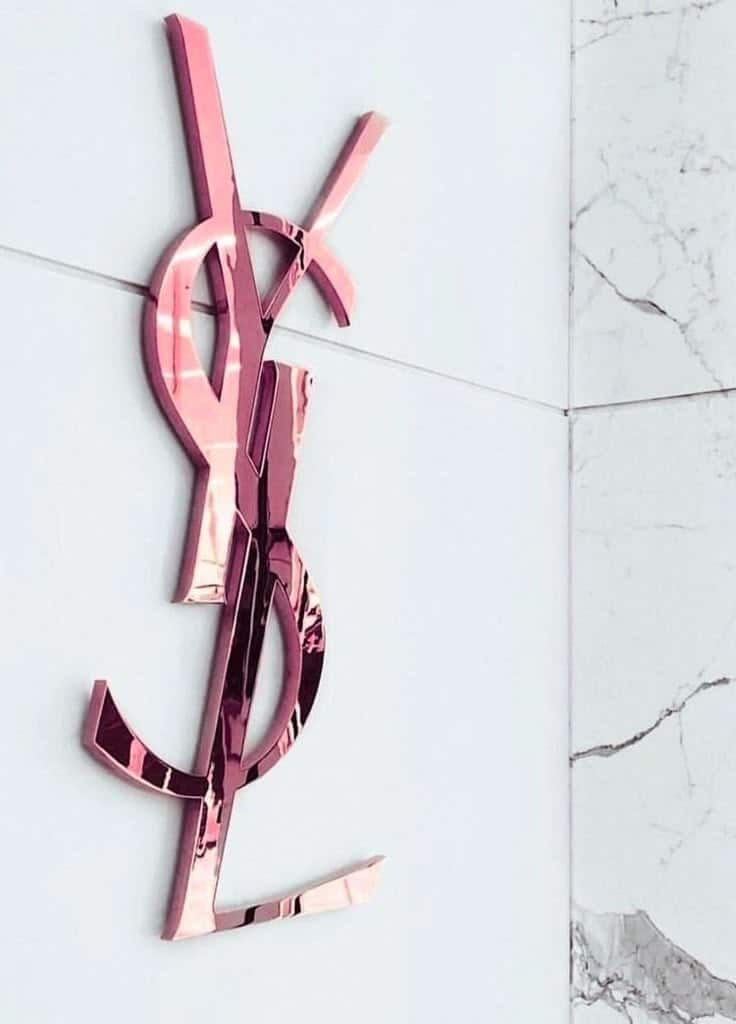 Pink YSL logo on a marble wall background. Elegant, reflective design.