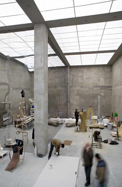 Artists working in a spacious, industrial-looking studio with high ceilings and modern art installations.