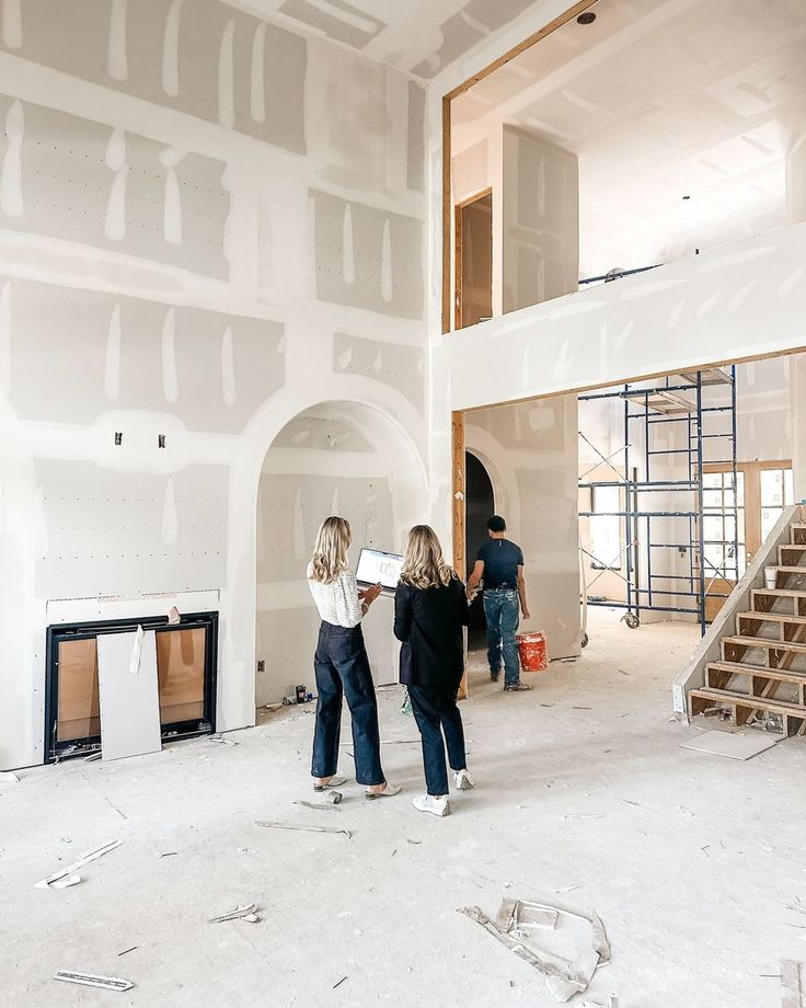 Two people reviewing construction plans inside a partially finished building with scaffolding and stairs.