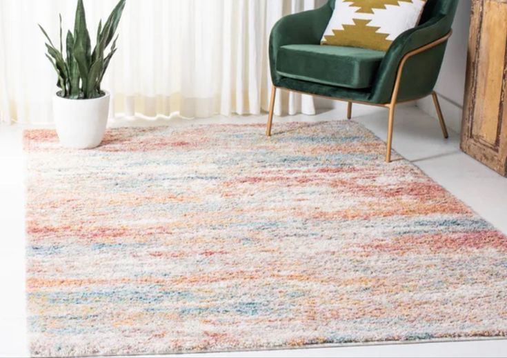 Colorful rug in a cozy room with a green chair and potted plant near a window with white curtains.