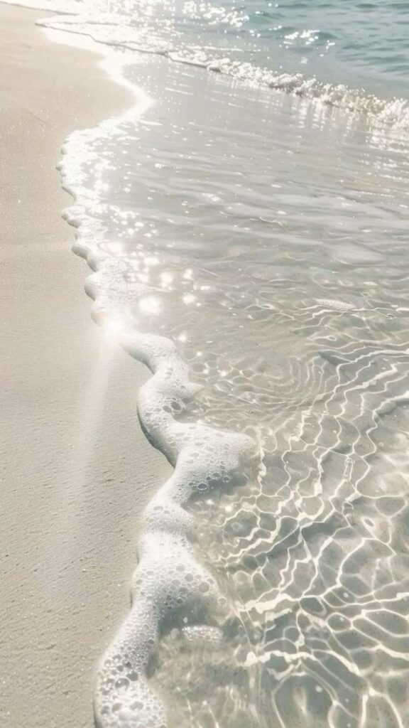 Waves gently lapping on a sunlit sandy beach, creating a serene and sparkling coastal scene.