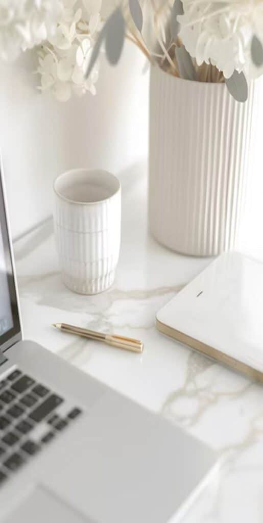 Modern workspace with laptop, tablet, coffee cup, and flowers on a marble desk. Minimalist office decor.