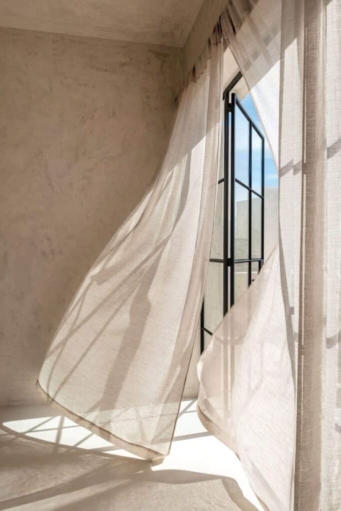 Sunny room with sheer curtains blowing in the breeze through an open window, creating a warm and airy atmosphere.