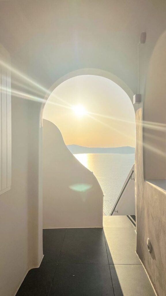 Sunlight streaming through an arched passageway, overlooking a serene ocean view during sunset.