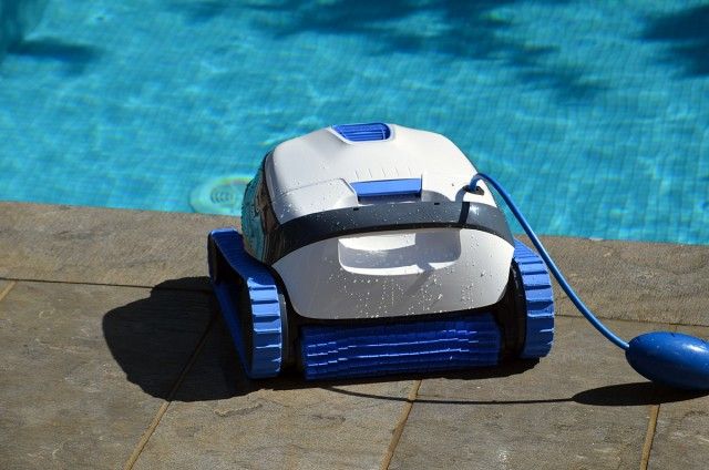 Robotic pool cleaner on the edge of a blue swimming pool, ready for automated cleaning.