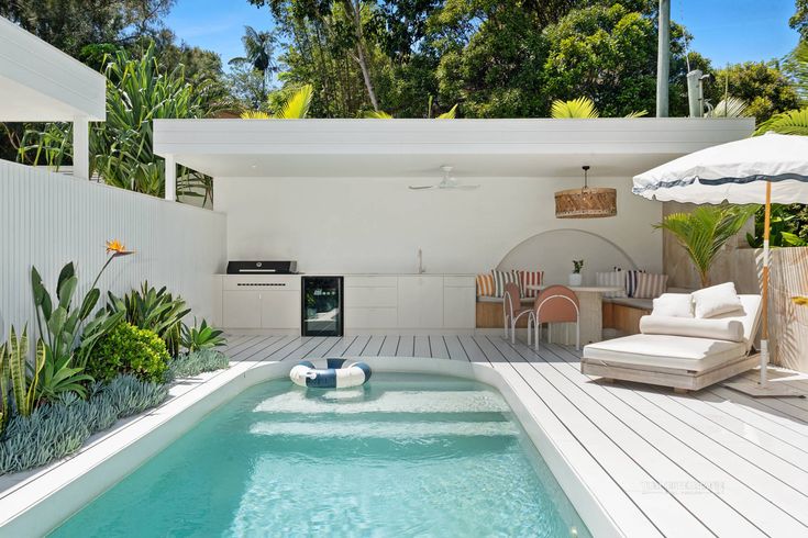 Modern outdoor pool area with lounge chairs, green plants, and a sleek kitchen setup under a minimalist pergola.
