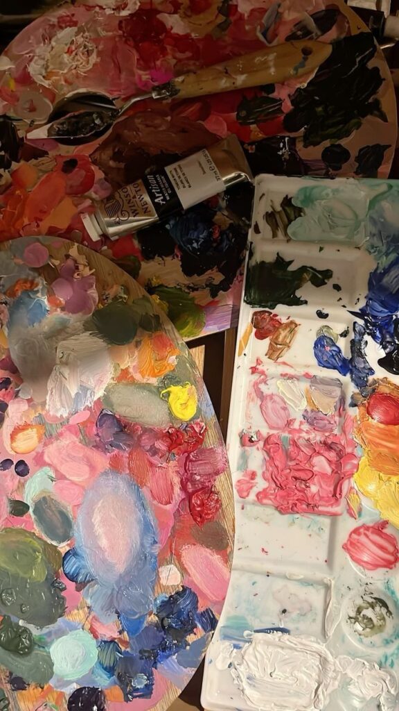 Colorful artist palettes with mixed oil paints and tools on a table, showcasing vibrant creativity and art supplies.