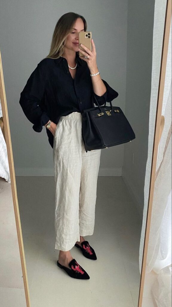 _ - 2025-05-21T104420872 Stylish woman in black shirt and beige pants takes a mirror selfie, holding a black handbag, showcasing chic fashion attire. | Sky Rye Design Stylish woman in black shirt and beige pants takes a mirror selfie, holding a black handbag, showcasing chic fashion attire.
