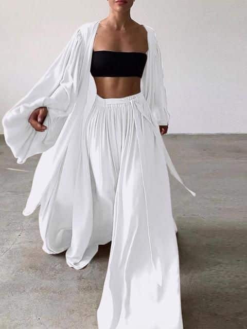 Fashionable woman in flowing white outfit with black top, showcasing style and elegance while walking indoors.