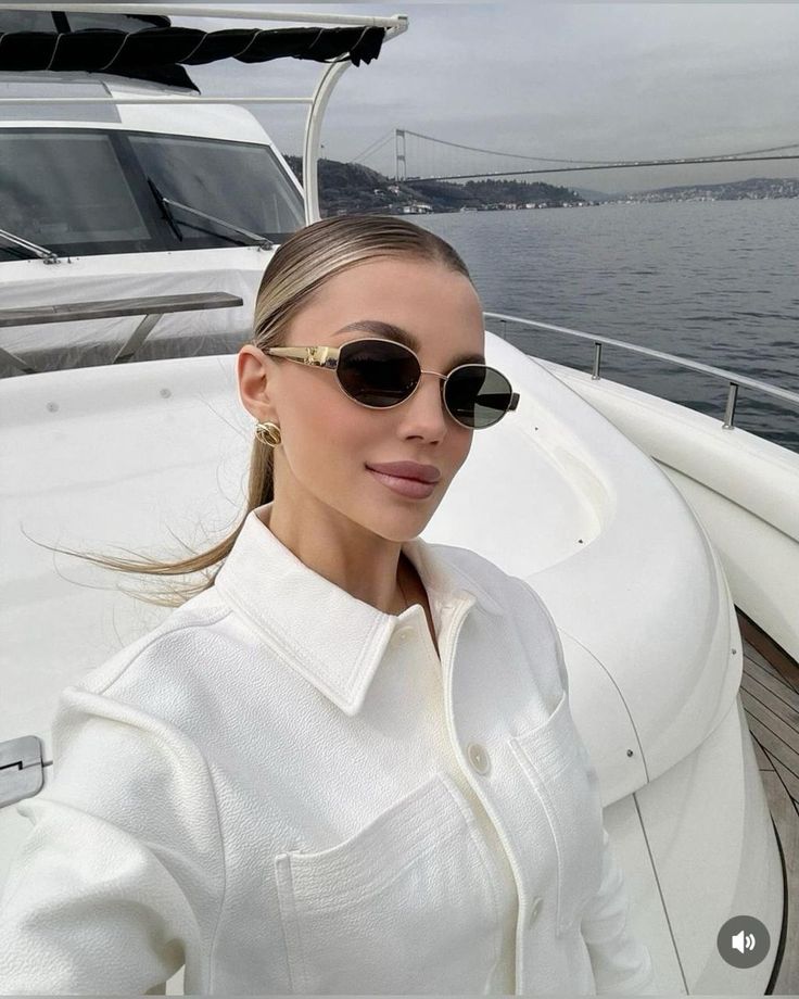 Woman in sunglasses enjoying a yacht ride with a scenic bridge and water view in the background.