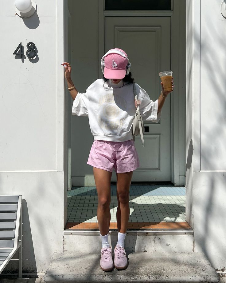 Person in white sweatshirt and pink shorts enjoys iced coffee outside.