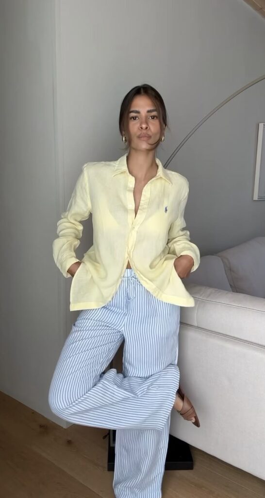 Woman in a yellow shirt and striped pants posing casually indoors.