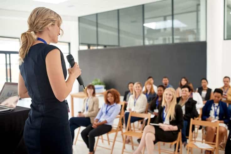 Woman presenting to an attentive audience in a conference room.