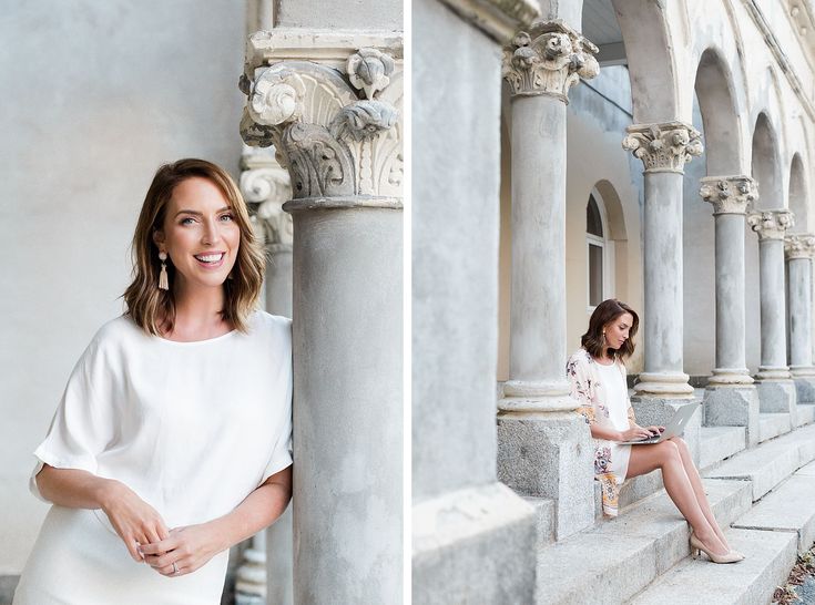 Woman in white by elegant columns, smiling and working on a laptop, showcasing casual elegance and productivity.