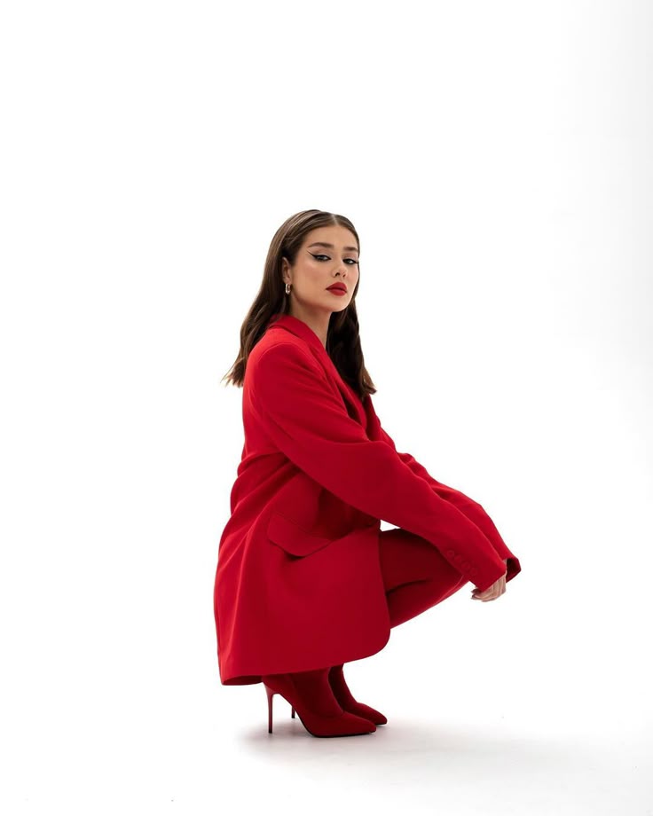 Woman in stylish red outfit and boots posing confidently against white background.