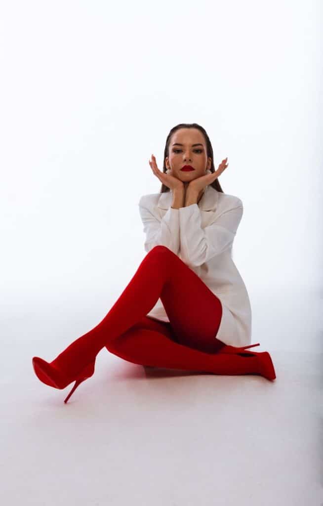 Woman in red stockings and white blazer poses stylishly against a white backdrop.