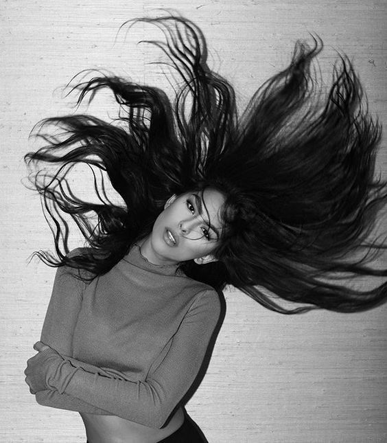 Woman with long flowing hair lying down, wearing a sweater, black and white photography, expressive motion.