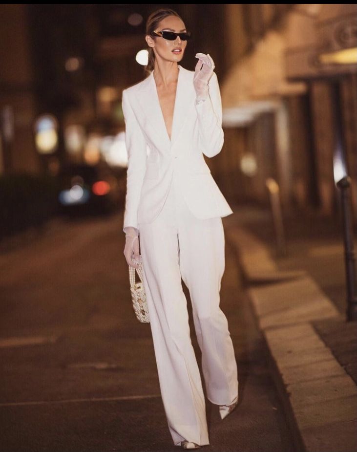 Stylish woman in a white suit and sunglasses walking confidently down a city street at night.