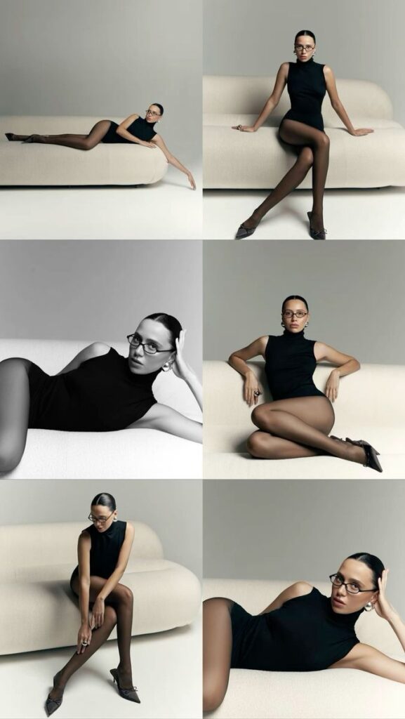 Stylish woman in black outfit and glasses posing on a beige sofa, showcasing modern elegance and fashion.