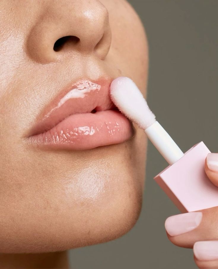 Close-up of glossy lips being applied with pink lip gloss using an applicator.