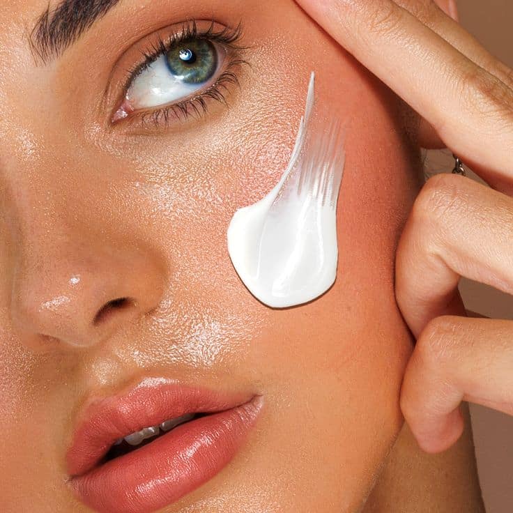 Woman applying moisturizing cream on cheek for flawless skin care.
