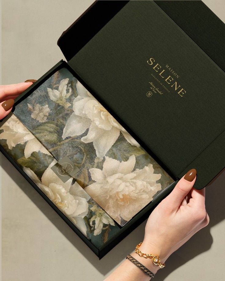 Elegant floral print fabric in a Maison Selene box held by manicured hands with gold bracelet.
