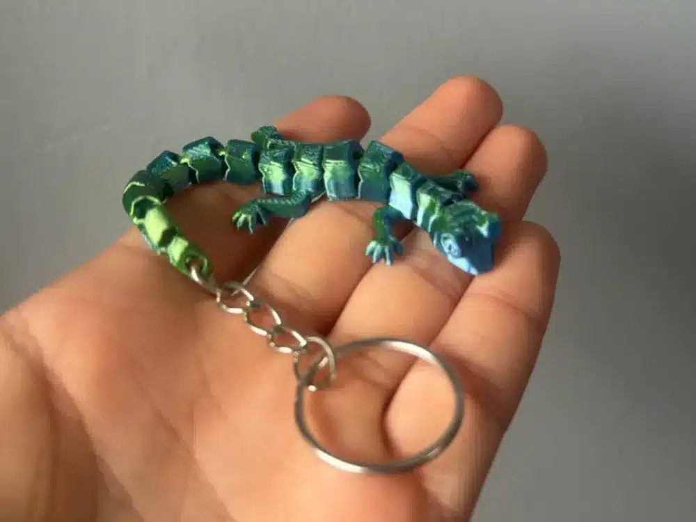 Hand holding a colorful 3D-printed lizard keychain with intricate details and a metallic ring.