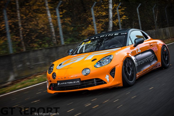 Orange Alpine sports car racing on a track, showcasing speed and performance, with autumn trees in the background.