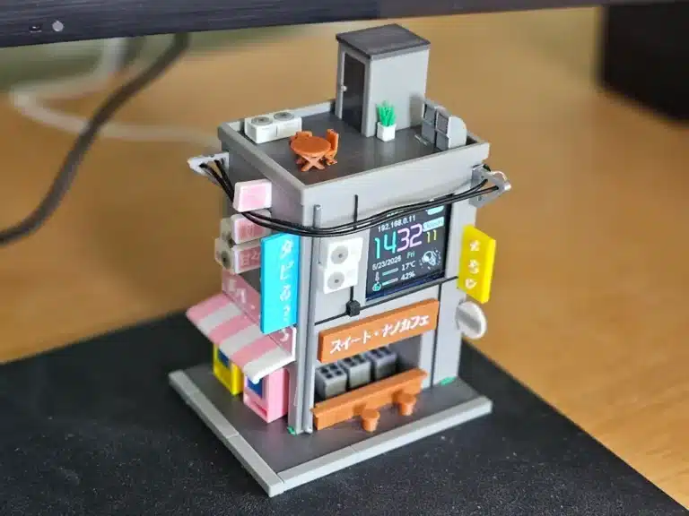 2025-05-23_fe58eb48e6aa98 Miniature building model with digital display on desk; detailed rooftop, signs, and colorful storefronts. | Sky Rye Design Miniature building model with digital display on desk; detailed rooftop, signs, and colorful storefronts.