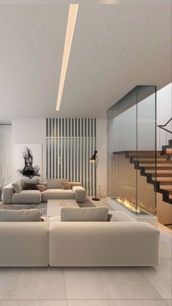 Modern living room with beige sofas, abstract art, and glass fireplace next to a staircase.