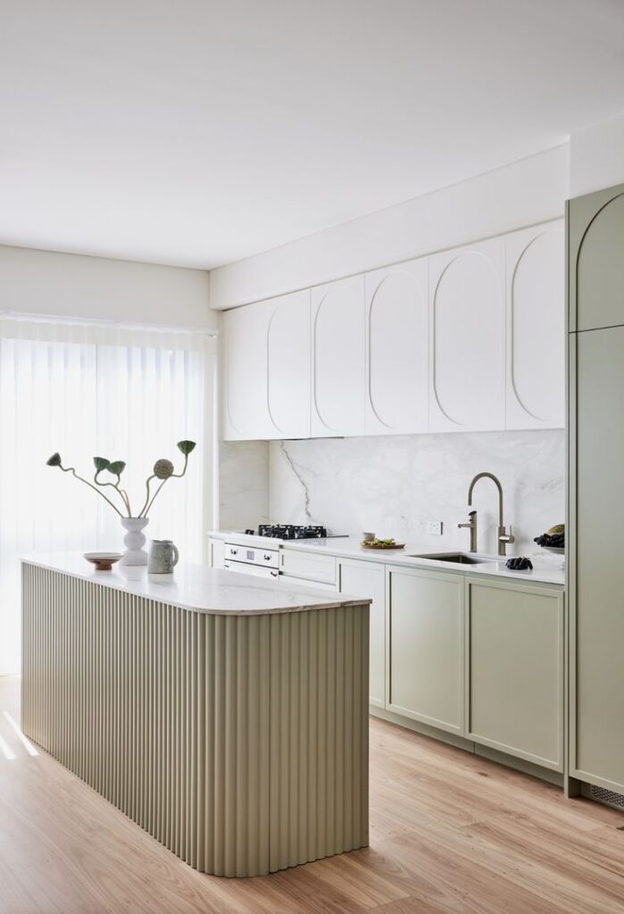 Modern kitchen with white cabinets, a marble backsplash, and a ribbed island. Minimalist decor and wood flooring.