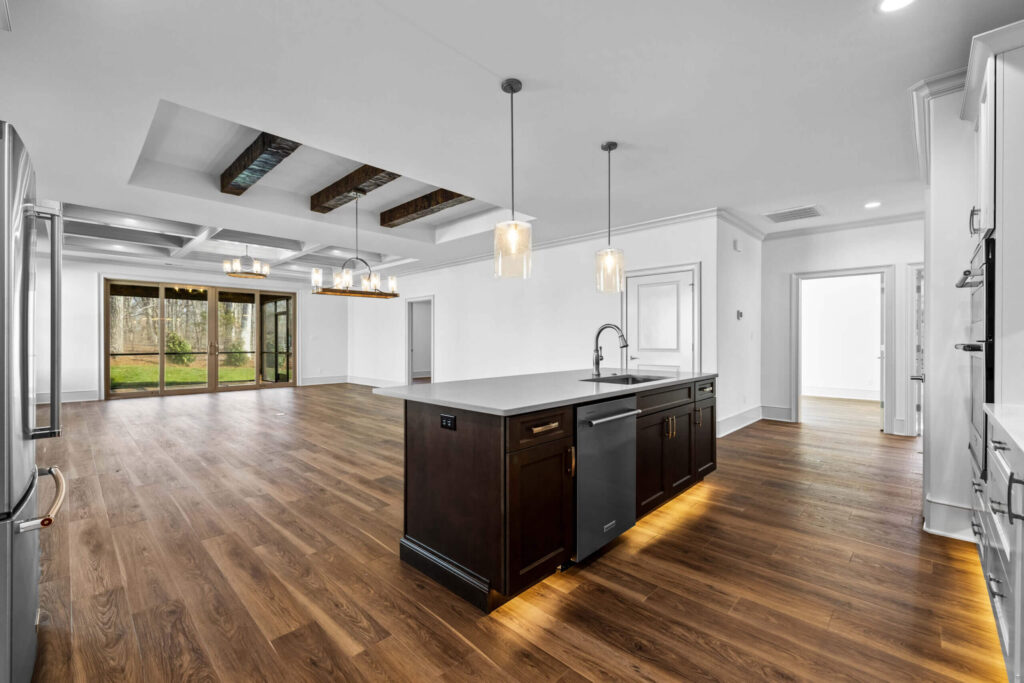 Modern open-plan kitchen and living space with hardwood floors, recessed lighting, and large sliding glass doors.