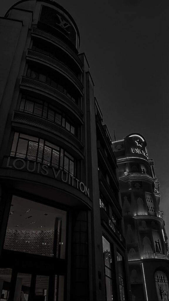Louis Vuitton and Dior buildings at night with glowing signs, showcasing luxury brands and architectural elegance.