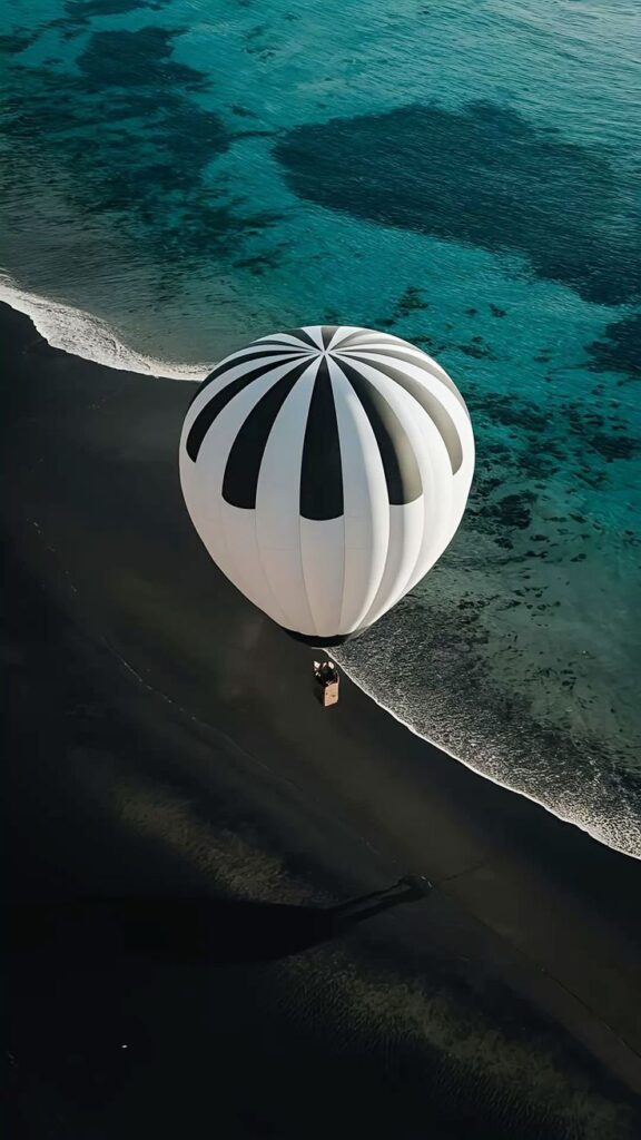 Aerial view of a hot air balloon on a black sand beach by the turquoise ocean.