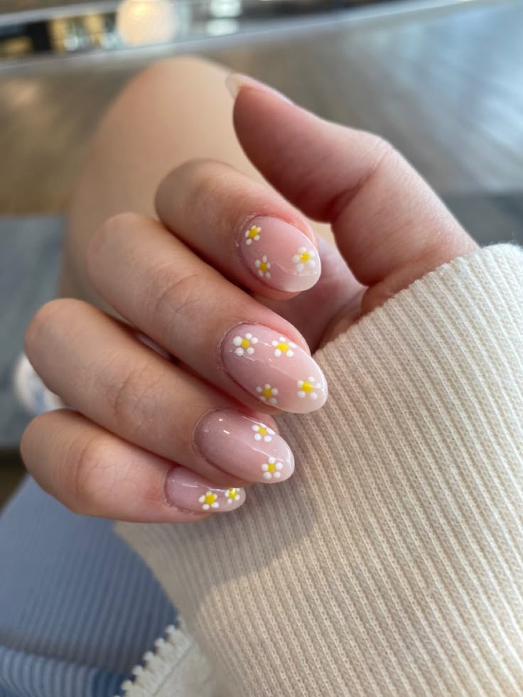 Close-up of a hand with pink nails featuring delicate white and yellow flower nail art.