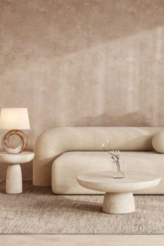 Minimalist beige living room with a modern sofa, round table, and decorative lamp on a textured rug.