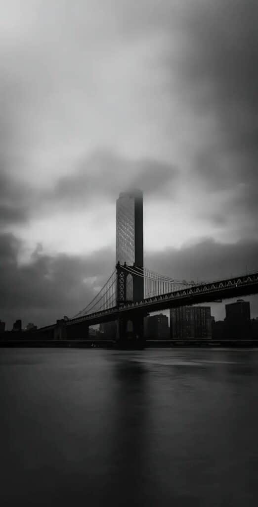 Moody skyline with a bridge and tall building in foggy, monochrome setting.