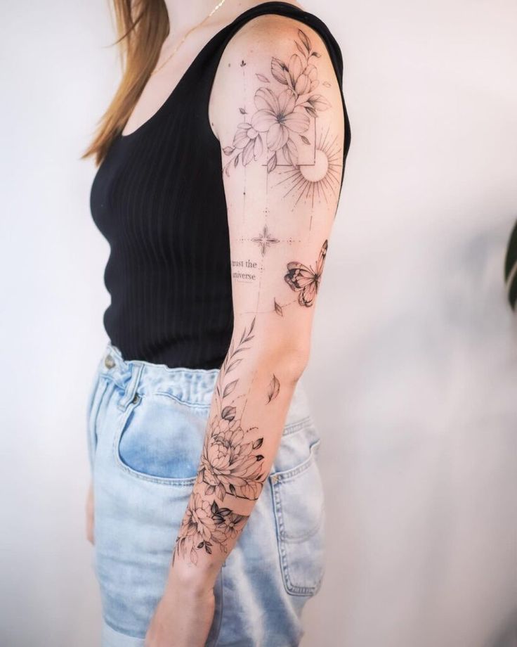 Woman with intricate floral and butterfly tattoo sleeve wearing black top and denim shorts.