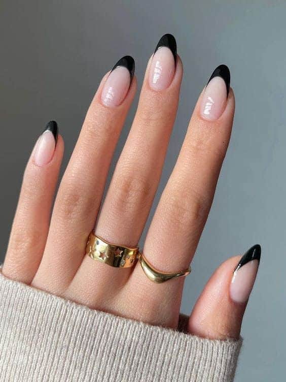 Chic hand with black French manicure, gold rings, and a beige sweater.