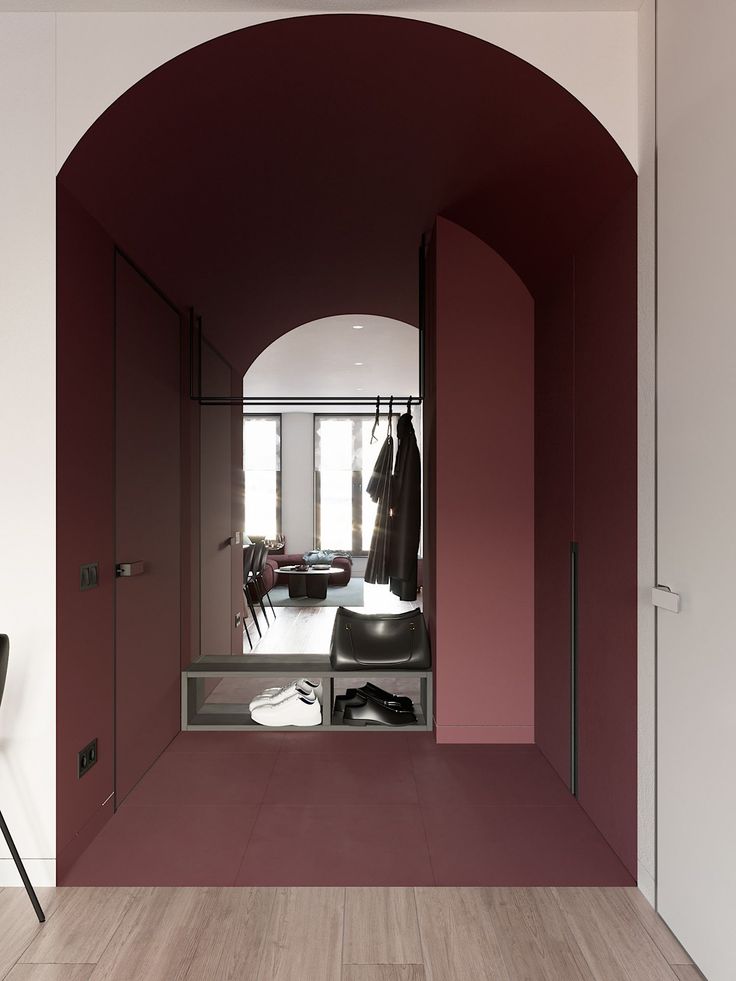 Modern hallway with arched doorway, burgundy walls, coat rack, and shoe storage, leading to a bright living area.