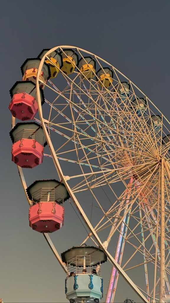 Colorful Ferris wheel at sunset, with vibrant cabins against a twilight sky, showcasing amusement park fun.