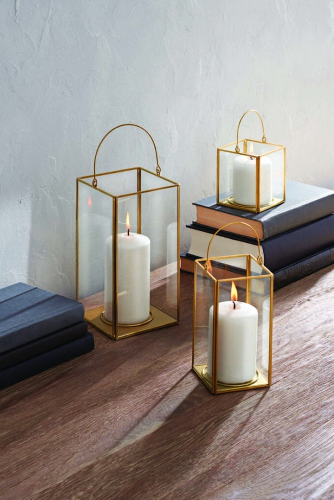 Three decorative lanterns with lit candles on a wooden table beside stacked books, adding warmth and charm to the space.