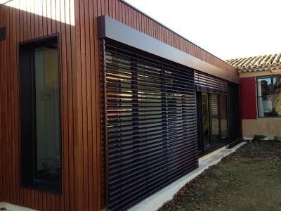 Modern house exterior with wooden siding and large black slatted window, showcasing contemporary architectural design.