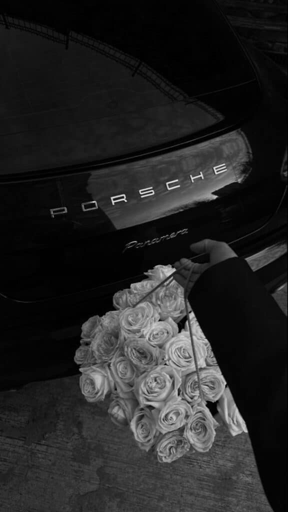 Person holding white roses by a black Porsche Panamera, reflecting luxury and elegance.