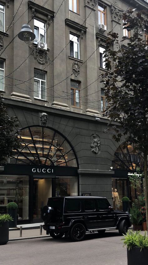 Luxury SUV parked outside Gucci store in a city street, showcasing fashion and style.