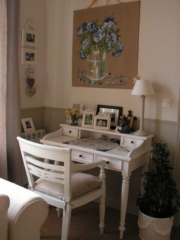 Cozy home office with vintage white desk, floral decor, and framed photos on a beige wall.