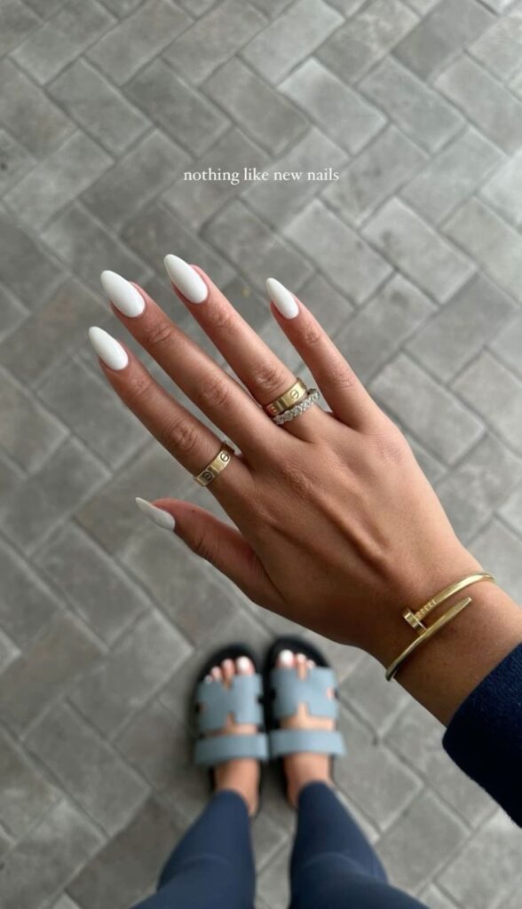 Elegant hand with white acrylic nails and gold jewelry on herringbone tiled floor.